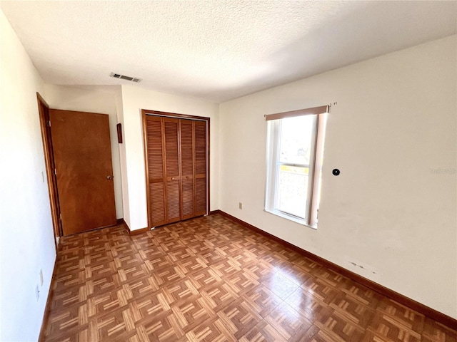 unfurnished bedroom featuring visible vents, baseboards, a textured ceiling, and a closet