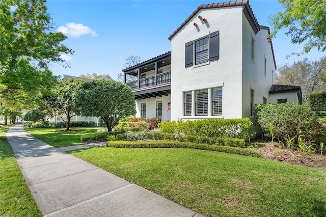 view of front of house featuring a balcony, stucco siding, a tile roof, and a front lawn