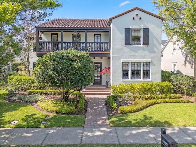 mediterranean / spanish-style home featuring stucco siding, a balcony, a front yard, and a tile roof