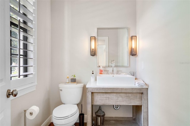 half bathroom with toilet, baseboards, and a sink