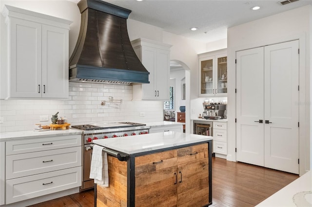 kitchen featuring premium range hood, dark wood finished floors, arched walkways, high end stove, and tasteful backsplash