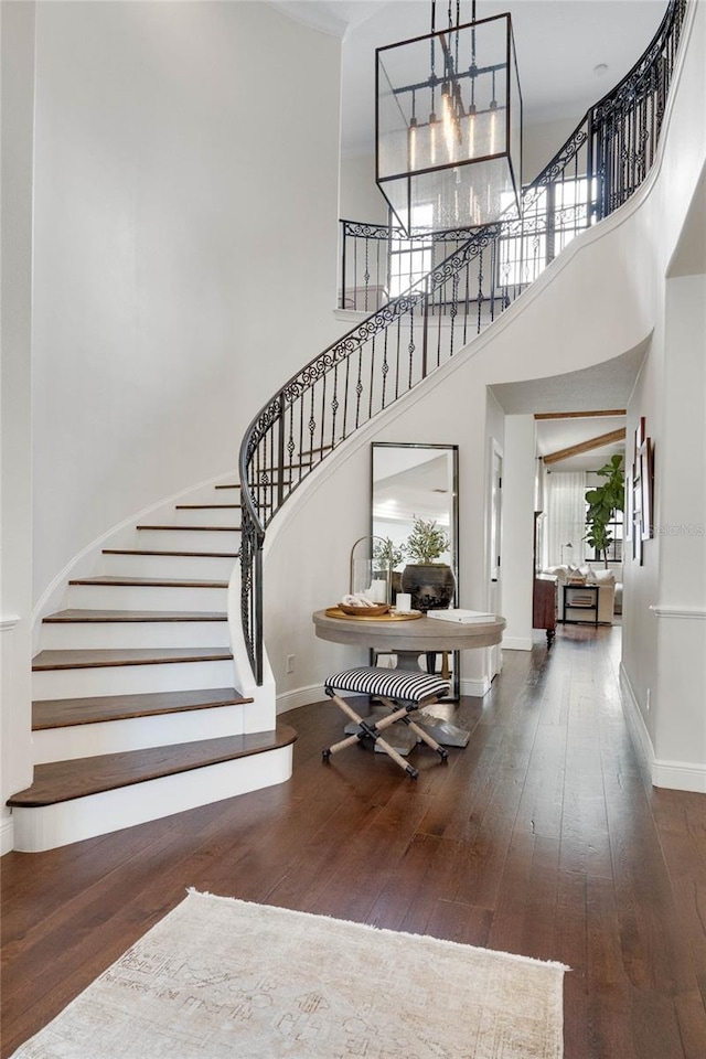 stairway featuring hardwood / wood-style floors, a high ceiling, a notable chandelier, and baseboards