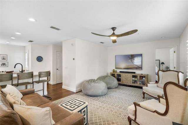 living area with visible vents, baseboards, wood finished floors, and a ceiling fan