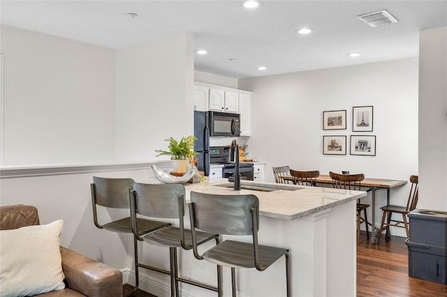 kitchen with visible vents, a peninsula, black microwave, a kitchen bar, and range