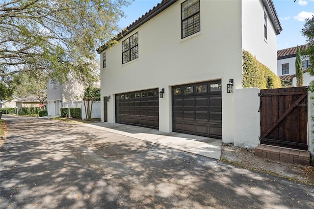 view of side of home with a tiled roof, a gate, a garage, and stucco siding