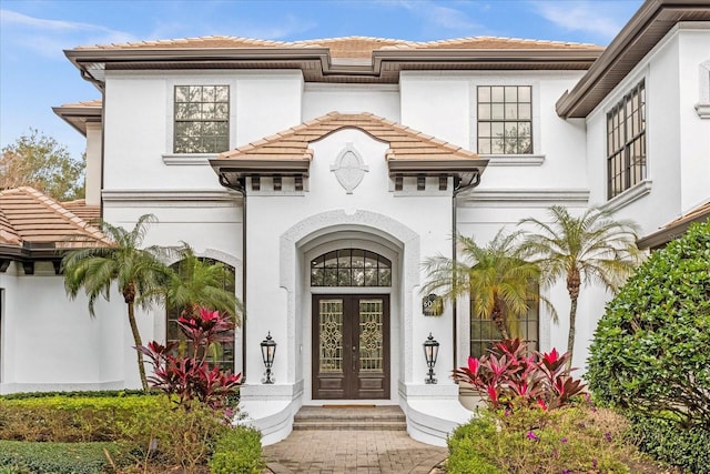 view of exterior entry with a tile roof, french doors, and stucco siding