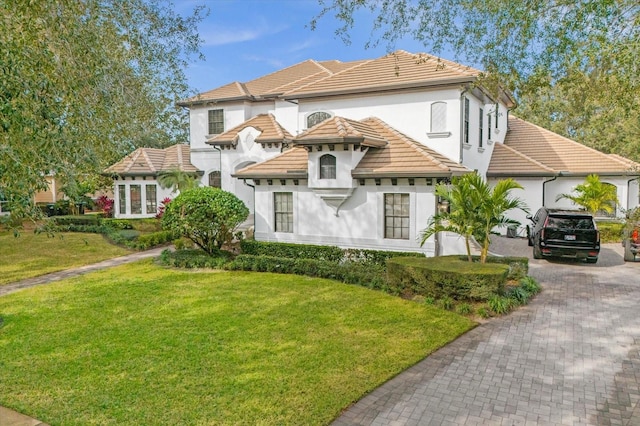 mediterranean / spanish-style house with stucco siding, a front lawn, a garage, a tiled roof, and decorative driveway