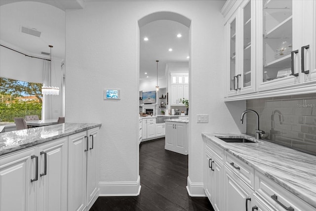 kitchen featuring visible vents, dark wood finished floors, arched walkways, white cabinetry, and a sink