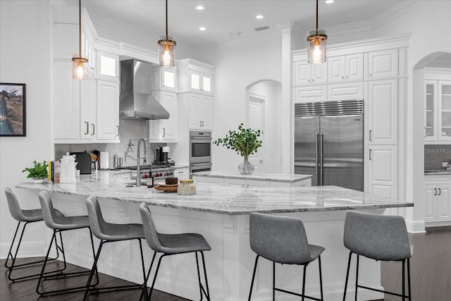 kitchen featuring backsplash, white cabinetry, stainless steel appliances, a peninsula, and wall chimney range hood