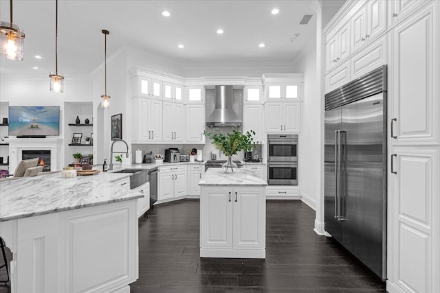 kitchen featuring visible vents, a peninsula, a sink, stainless steel appliances, and wall chimney range hood