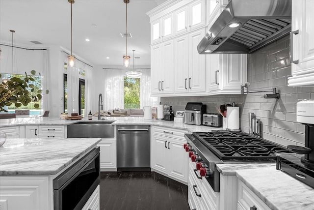 kitchen with a peninsula, stainless steel appliances, a sink, white cabinetry, and exhaust hood