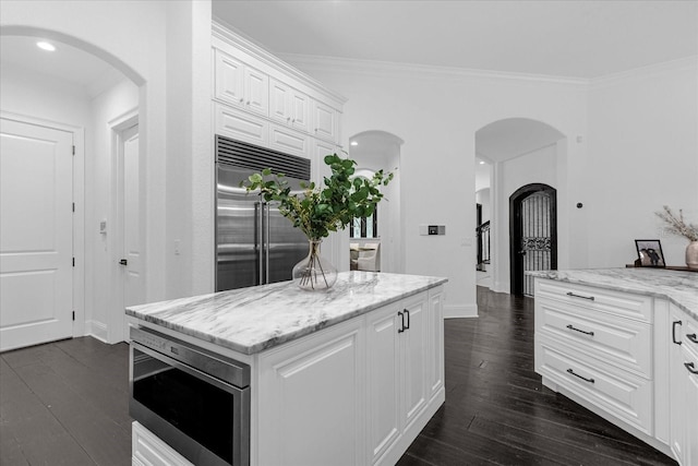 kitchen featuring arched walkways, built in appliances, white cabinetry, and dark wood-style flooring