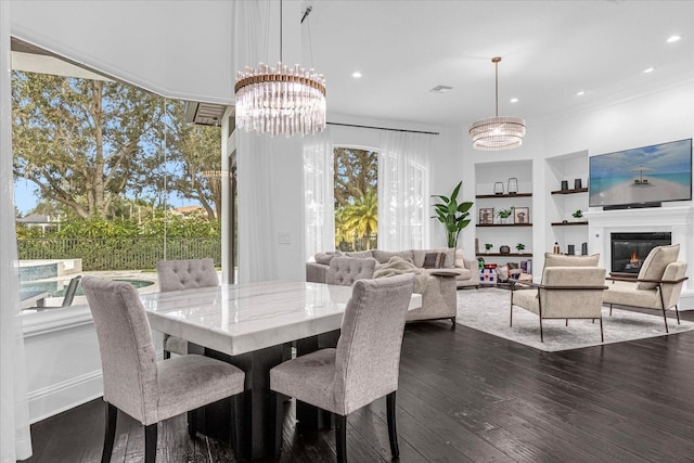 dining area featuring dark wood finished floors, a notable chandelier, plenty of natural light, and built in shelves