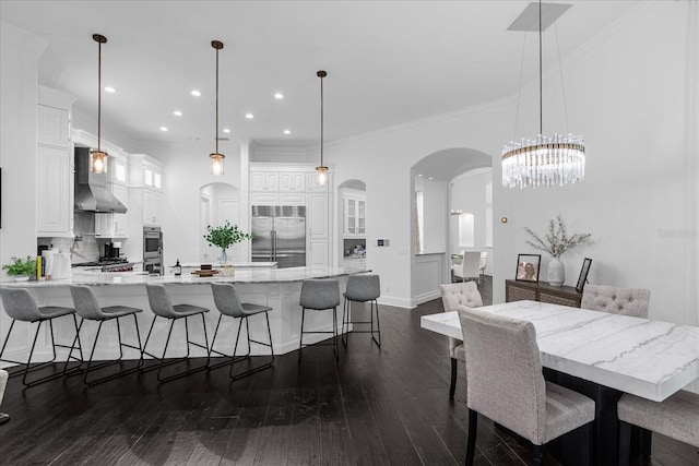 dining area with dark wood-type flooring, a notable chandelier, arched walkways, and ornamental molding