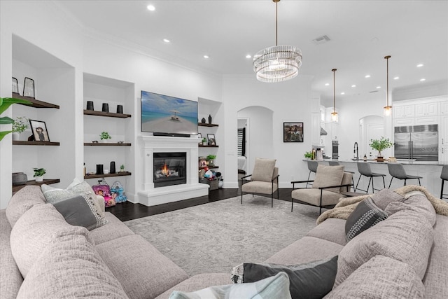 living area featuring arched walkways, built in shelves, dark wood-style flooring, and ornamental molding