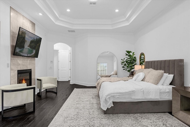 bedroom with visible vents, dark wood-type flooring, arched walkways, a fireplace, and crown molding