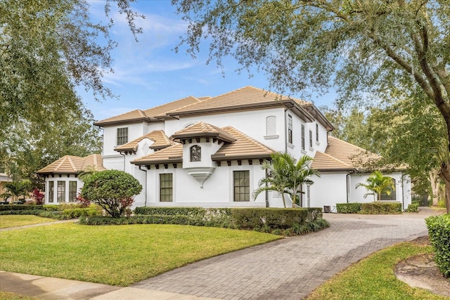 mediterranean / spanish home featuring stucco siding, a tile roof, decorative driveway, and a front yard