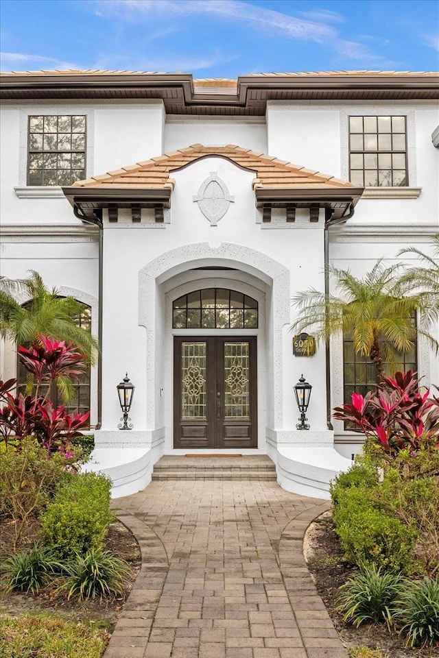 property entrance with french doors, stucco siding, and a tiled roof