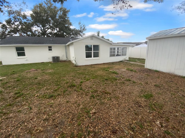 rear view of property with a yard, an outbuilding, central AC, and fence