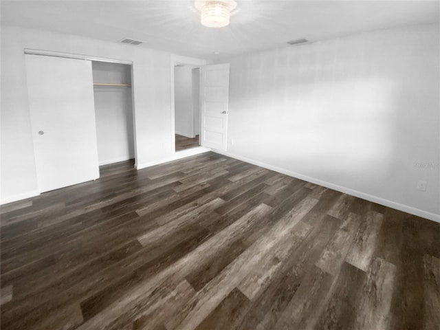 unfurnished bedroom with dark wood-type flooring, baseboards, visible vents, and a closet