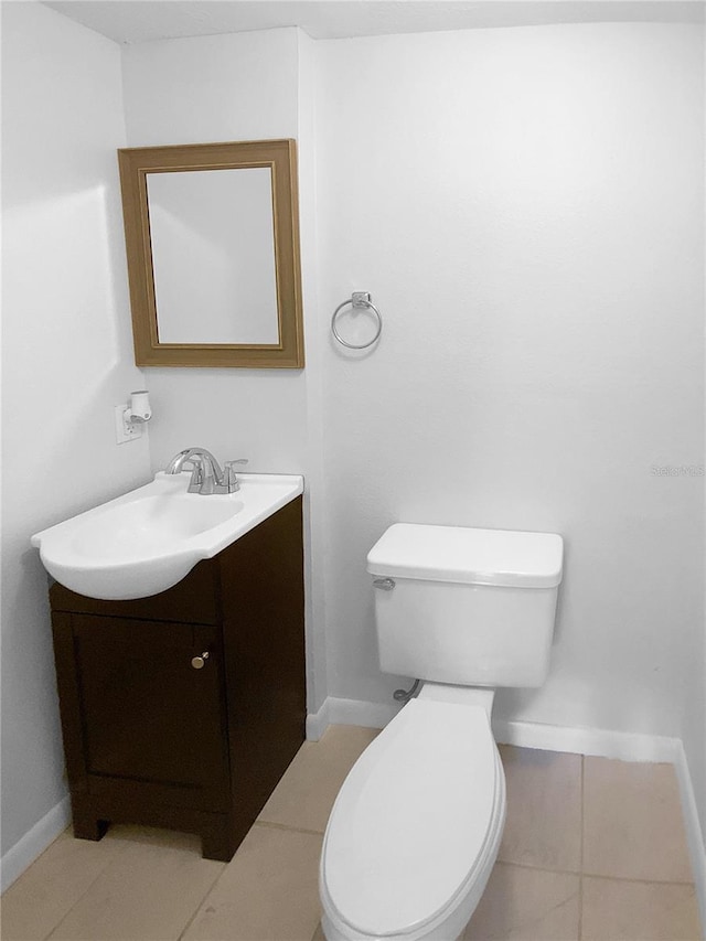 half bath with tile patterned flooring, toilet, vanity, and baseboards