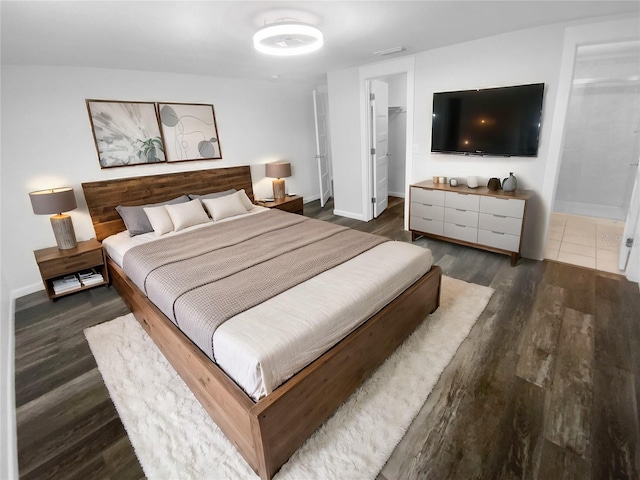 bedroom with a walk in closet, wood finished floors, baseboards, and a closet