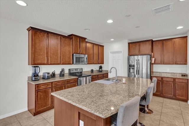 kitchen with visible vents, an island with sink, a sink, appliances with stainless steel finishes, and a breakfast bar area