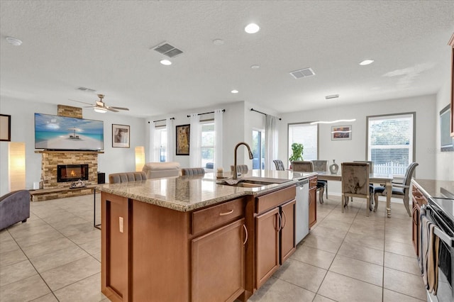 kitchen with visible vents, a sink, an island with sink, a fireplace, and stainless steel dishwasher