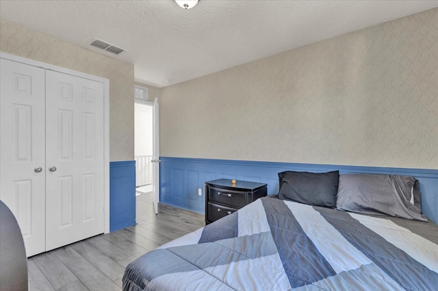 bedroom with wallpapered walls, a wainscoted wall, visible vents, and a textured ceiling