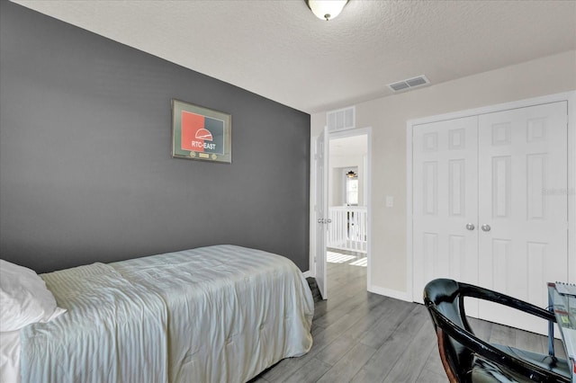 bedroom with wood finished floors, visible vents, a closet, and a textured ceiling