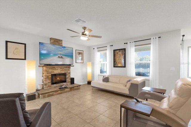 living room featuring light tile patterned floors, visible vents, a ceiling fan, and a fireplace