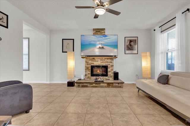 living area featuring light tile patterned floors, a stone fireplace, a ceiling fan, and baseboards