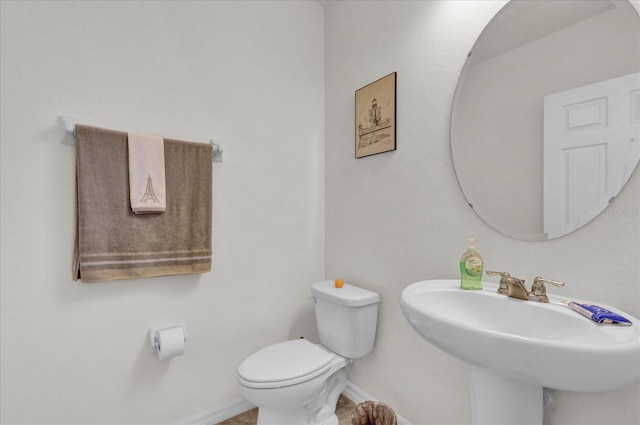 half bath featuring toilet, baseboards, and a sink