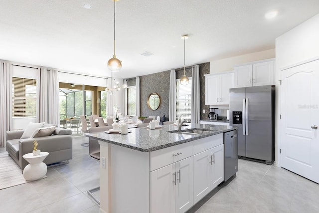 kitchen with a sink, dark stone countertops, open floor plan, stainless steel appliances, and white cabinets