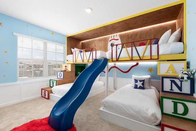 bedroom with carpet, wainscoting, and a decorative wall