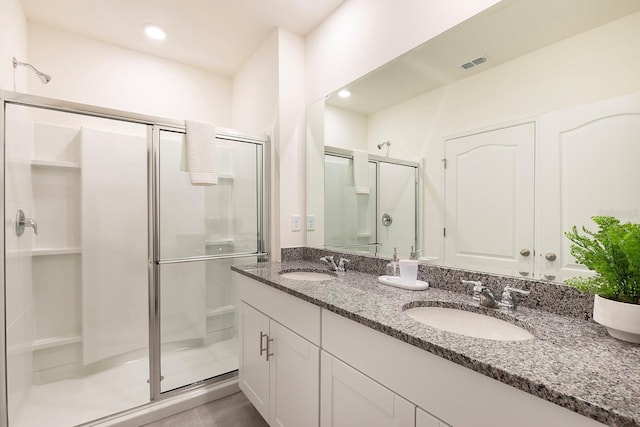 full bathroom with double vanity, visible vents, a shower stall, and a sink