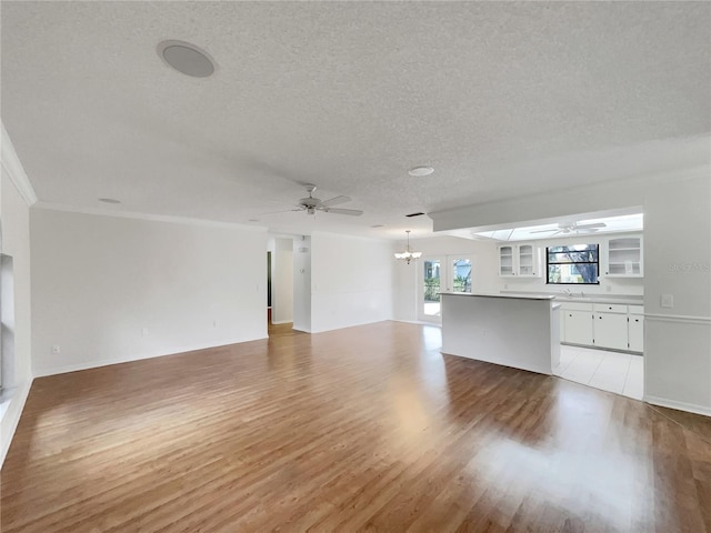 unfurnished living room featuring ceiling fan with notable chandelier, a textured ceiling, and light wood-type flooring