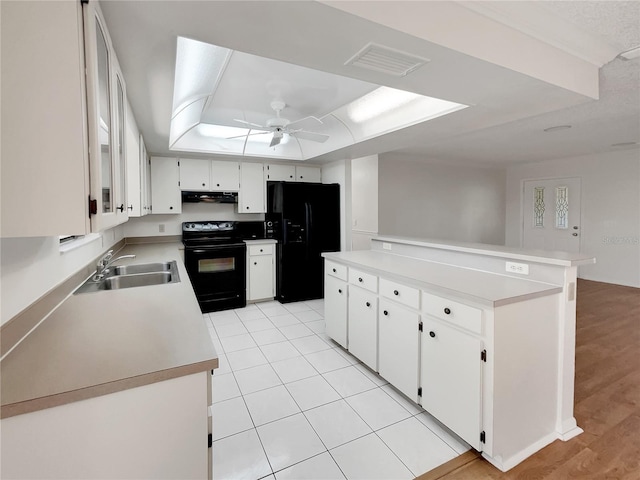 kitchen featuring visible vents, under cabinet range hood, black appliances, a raised ceiling, and a sink