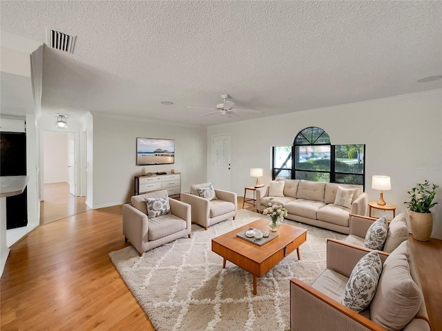 living area with visible vents, a textured ceiling, light wood-style floors, crown molding, and ceiling fan