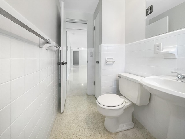 half bath featuring tile walls, wainscoting, toilet, and speckled floor