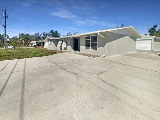 view of front facade featuring concrete driveway, a front yard, stucco siding, a garage, and an outbuilding