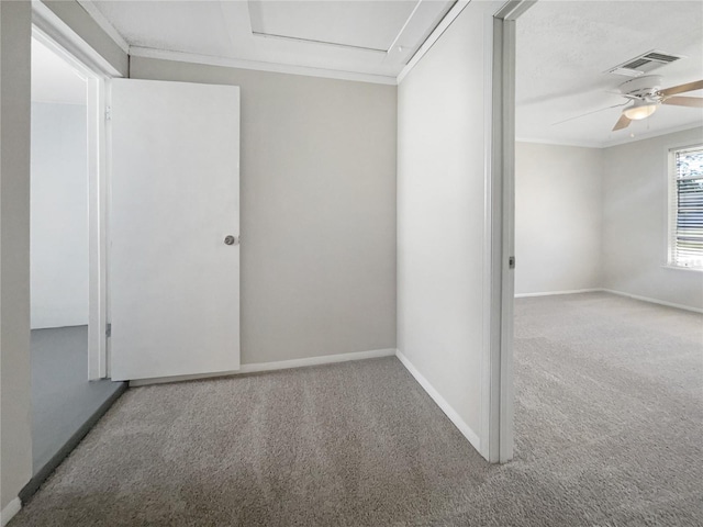 carpeted spare room with visible vents, baseboards, attic access, ornamental molding, and a ceiling fan