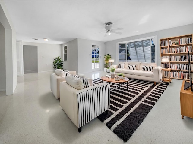 living area featuring speckled floor, a ceiling fan, and baseboards