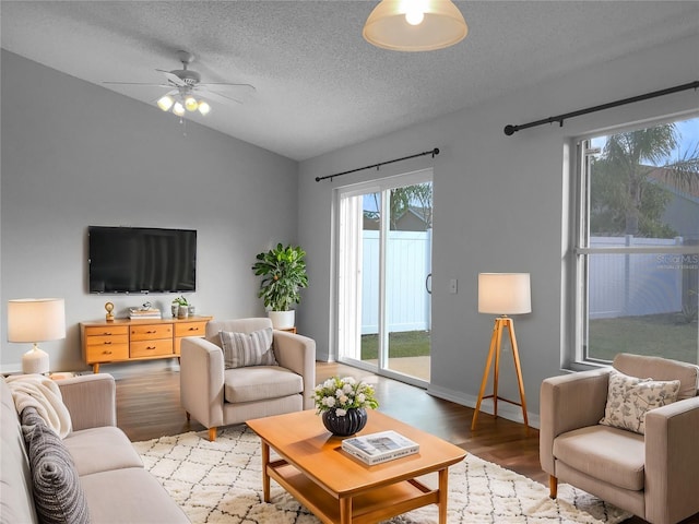 living room with lofted ceiling, light wood-style flooring, a ceiling fan, a textured ceiling, and baseboards