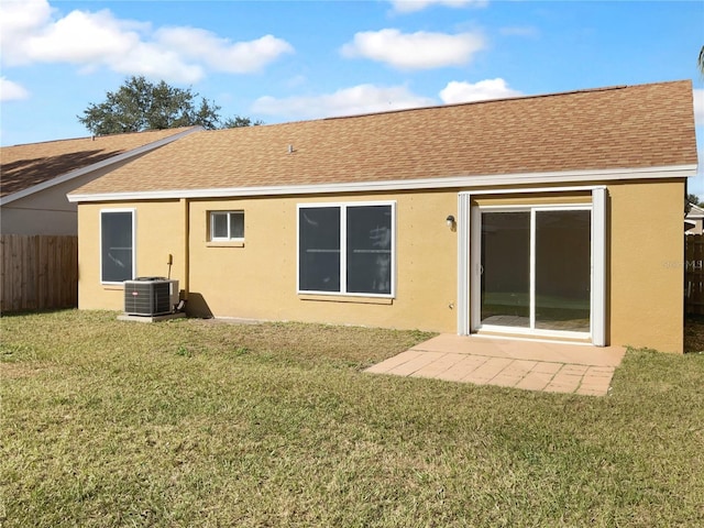 back of property with central AC unit, a lawn, roof with shingles, and fence