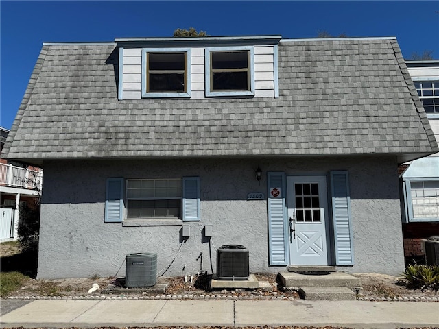 view of front of property with central AC unit, stucco siding, mansard roof, and a shingled roof