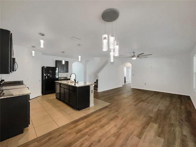 kitchen featuring arched walkways, a sink, black appliances, pendant lighting, and dark cabinets