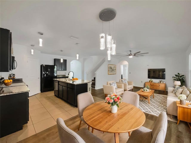 dining room with arched walkways, light tile patterned floors, stairway, and ceiling fan