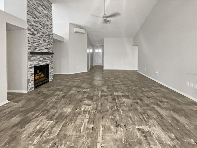 unfurnished living room featuring baseboards, ceiling fan, a wall mounted air conditioner, a fireplace, and wood finished floors