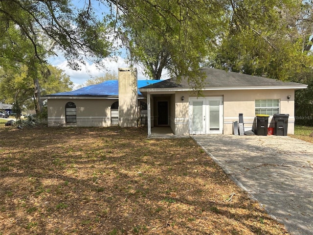 rear view of property with stucco siding, driveway, a chimney, and french doors